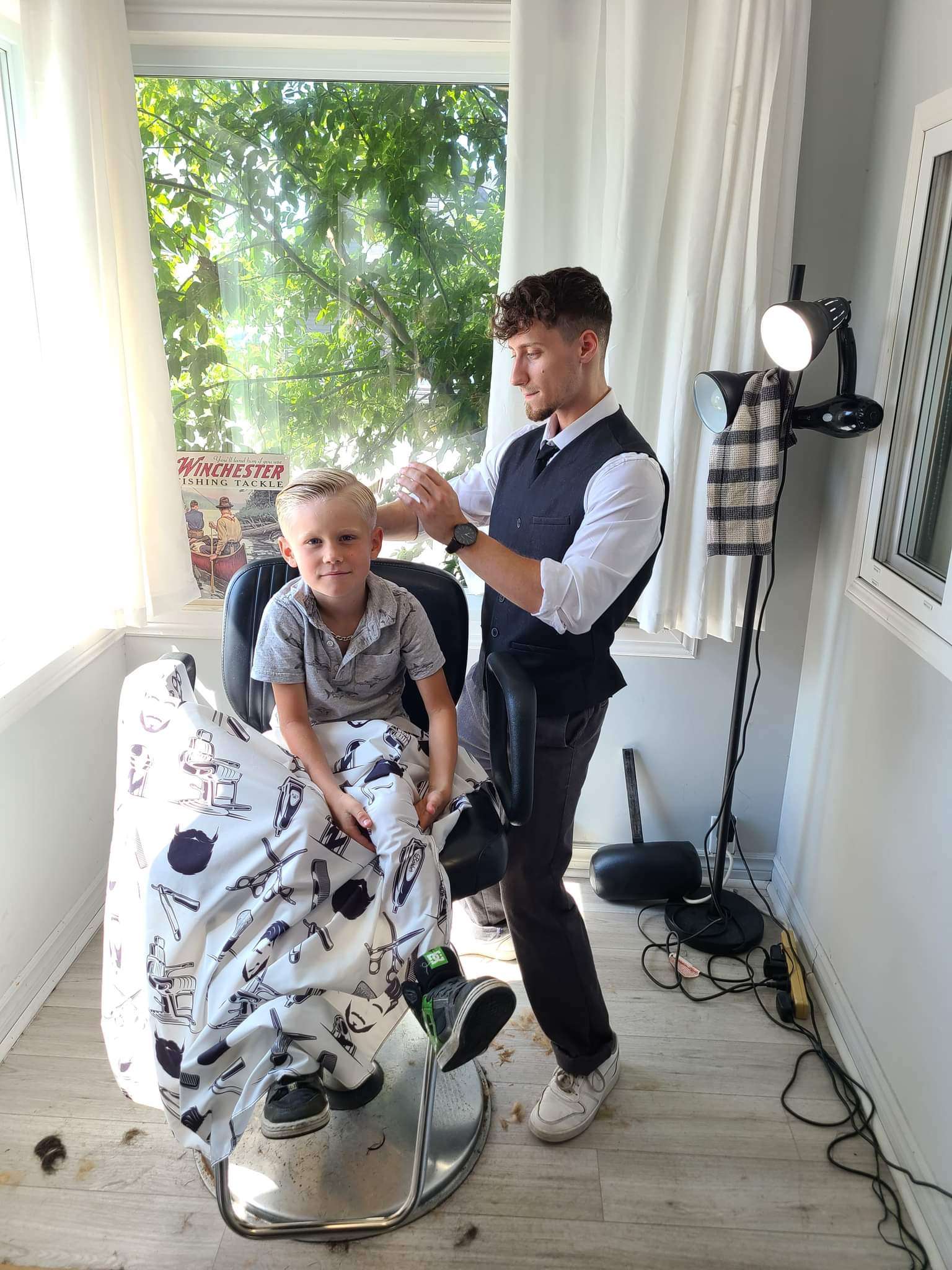 Olivier Lachapelle coupe les cheveux d'un jeune garçon blond assis sur la chaise de barbier qu'il a installée chez lui.